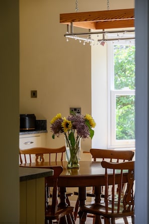 A dining area with a wooden table and chairs, a vase with flowers, and a window with greenery outside. - Bridge Farm -  a holiday cottage that sleeps 8 guests  in 3 bedrooms (Hartoft)