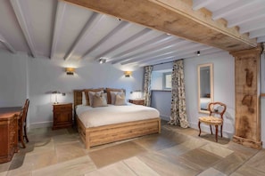 Ein Schlafzimmer mit einem hölzernen Bett, zwei Nachttischen mit Lampen, einem Sessel, einem Spiegel und einem Fenster mit Vorhängen.