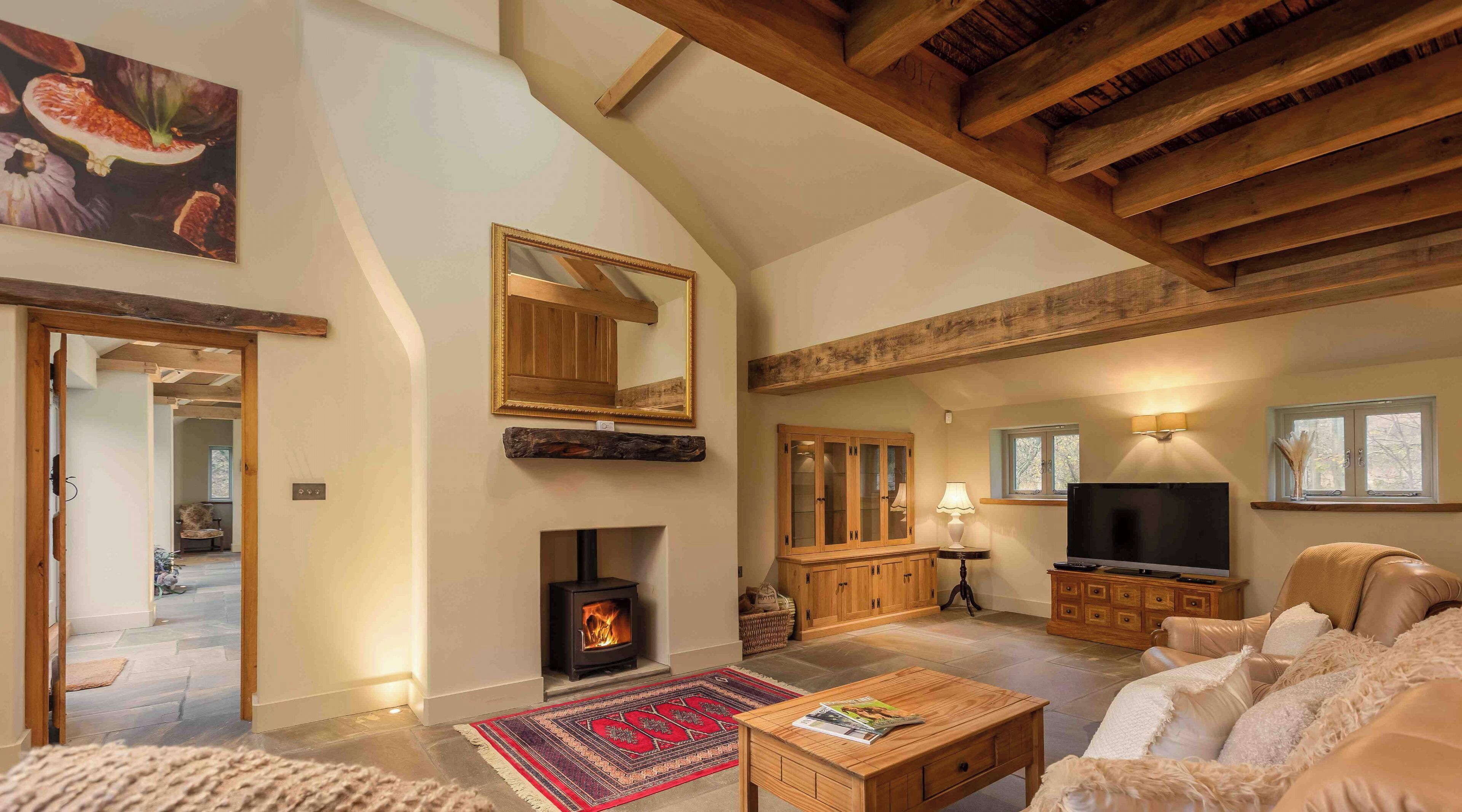 A spacious living room with a fireplace, wooden beams, a television, and a comfortable seating area.