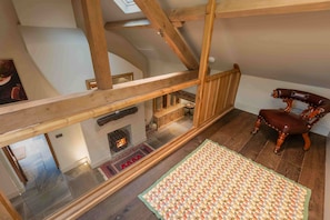 Ein Zimmer mit hohen Decken, freiliegenden Holzbalken, einem Kamin, einer hölzernen Bank und einem gemusterten Teppich.
