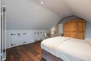 A bedroom with a large bed, wooden wardrobe, and a built-in bathtub. - Scugdale -  a holiday cottage that sleeps 4 guests  in 2 bedrooms (Hartoft)