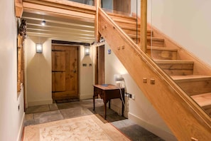 Eine Holztreppe führt zu einer oberen Etage, eine Holztür, ein kleiner Tisch mit einer Lampe und ein gemustertes Teppich im Raum.