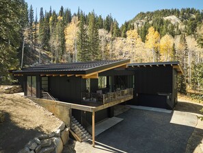Ein modernes, zweistöckiges Haus mit einer überdachten Terrasse und einer Steinmauer.