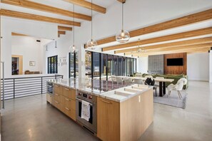 Eine moderne Küche mit einer zentralen Kochinsel, Holzbalken an der Decke und Pendelleuchten.