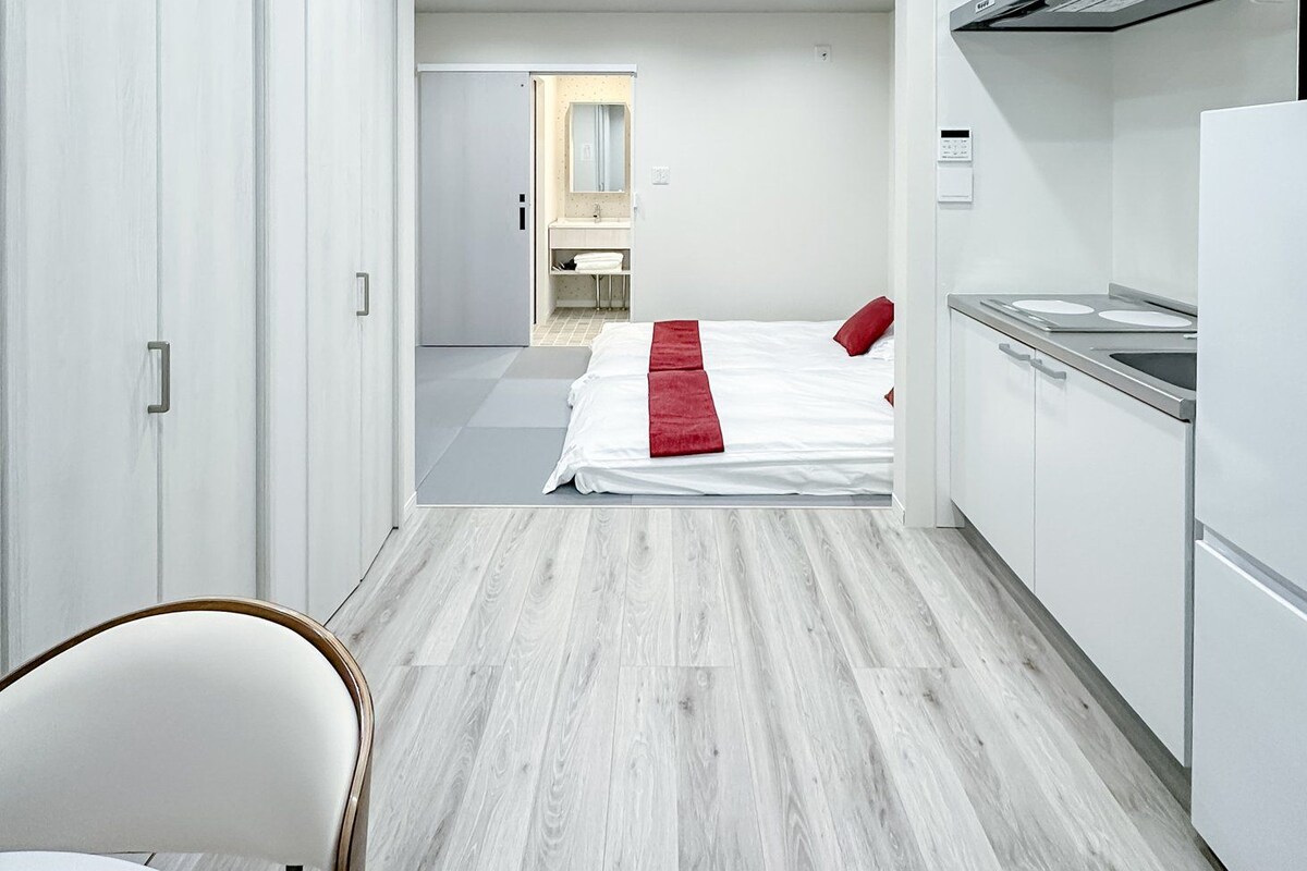 A modern hotel room with a bed, a kitchenette, and a bathroom.