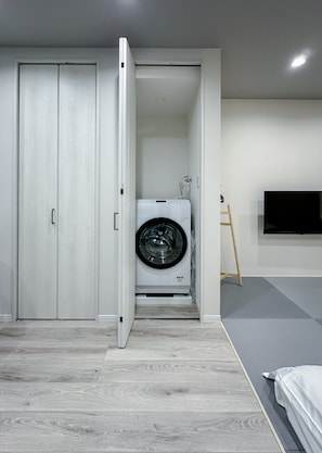 A room with a built-in washer and dryer, a wooden floor, and a TV mounted on the wall. - HANASTAY HIKARI (Osaka)