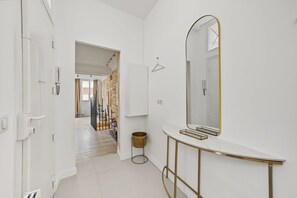 Een hal met een witte deur, een spiegel en een console tafel met gouden lijst.