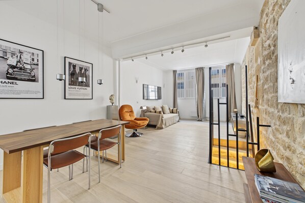 Een moderne woonkamer met een houten eettafel, stoelen, een bank en een groot raam met gordijnen.