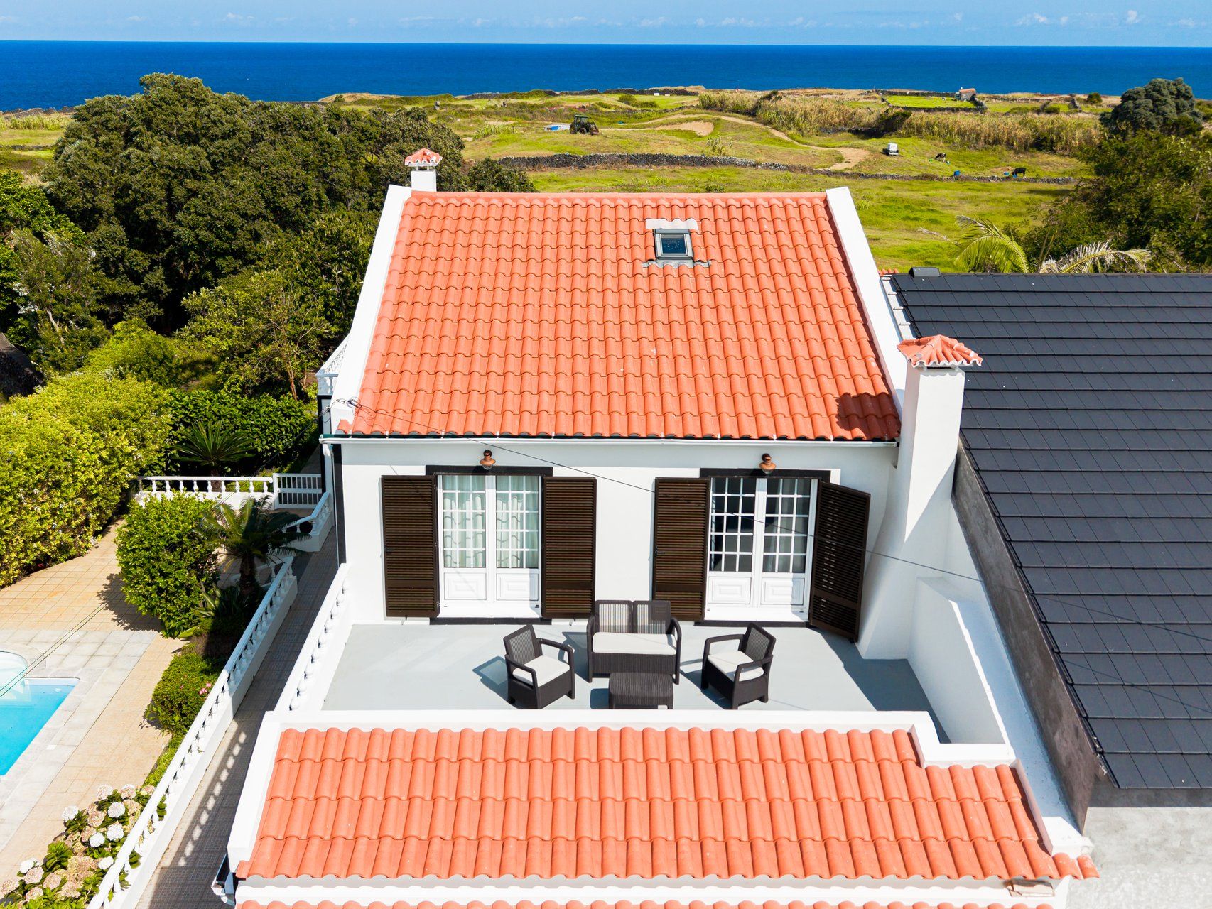 A two-story house with a red-tiled roof, a swimming pool, and a view of the ocean.