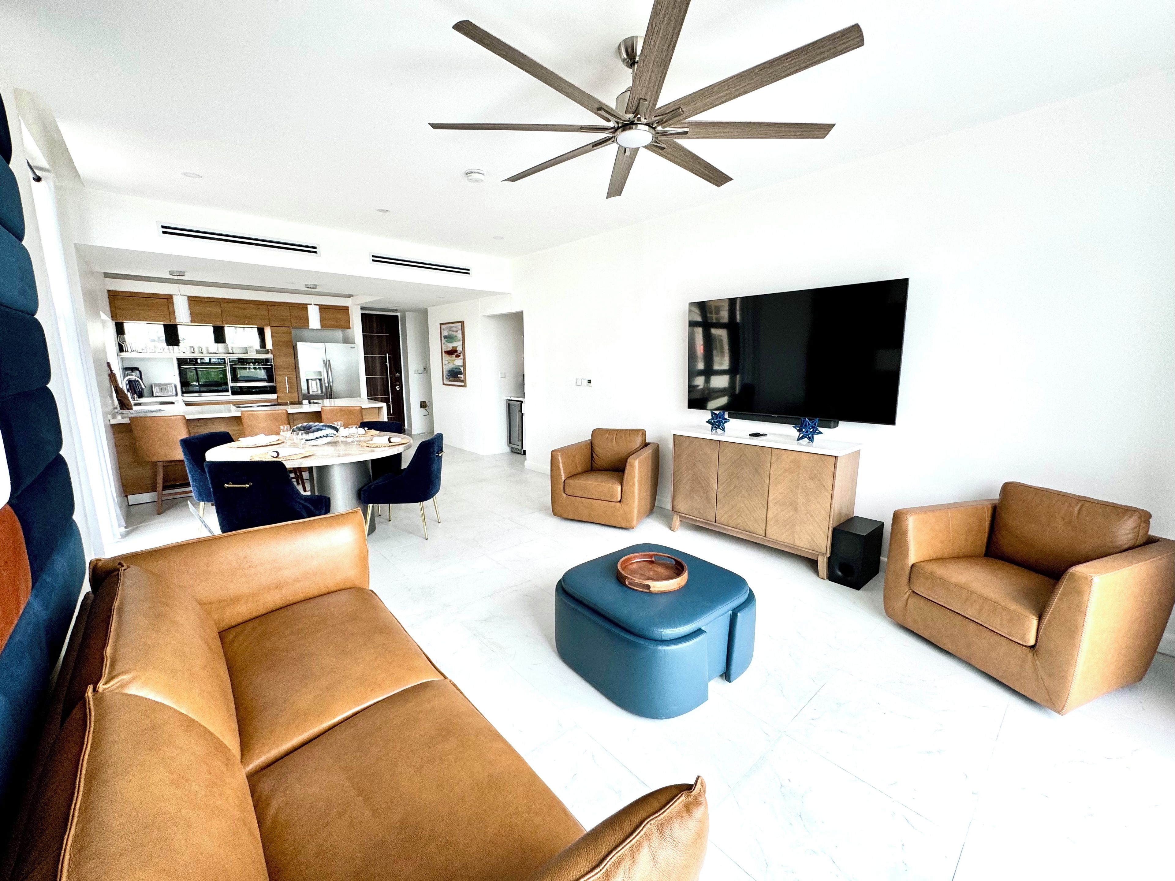 A modern living room with a ceiling fan, a flat-screen TV, and a dining area with chairs and a table.