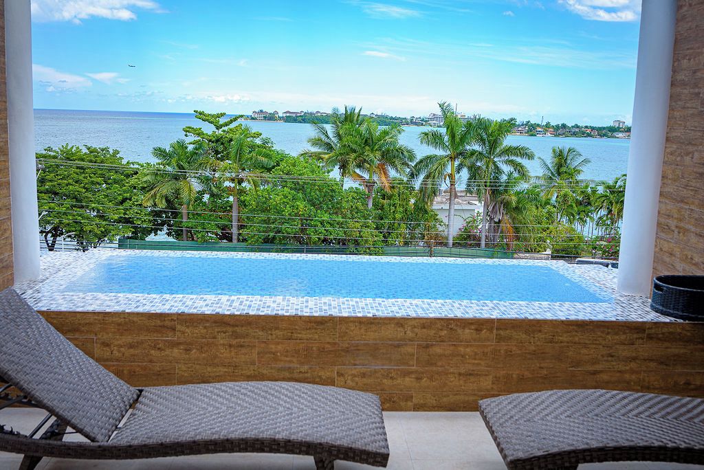 Vista de uma varanda com piscina, espreguiçadeiras e vista para o mar e palmeiras.