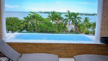 Vista de uma varanda com piscina, espreguiçadeiras e vista para o mar e palmeiras.