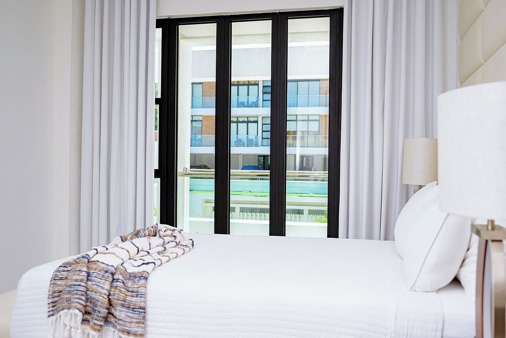 Quarto de hotel com uma cama grande, vista de um edifício com varandas e uma piscina.