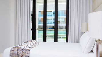 Quarto de hotel com uma cama grande, vista de um edifício com varandas e uma piscina.