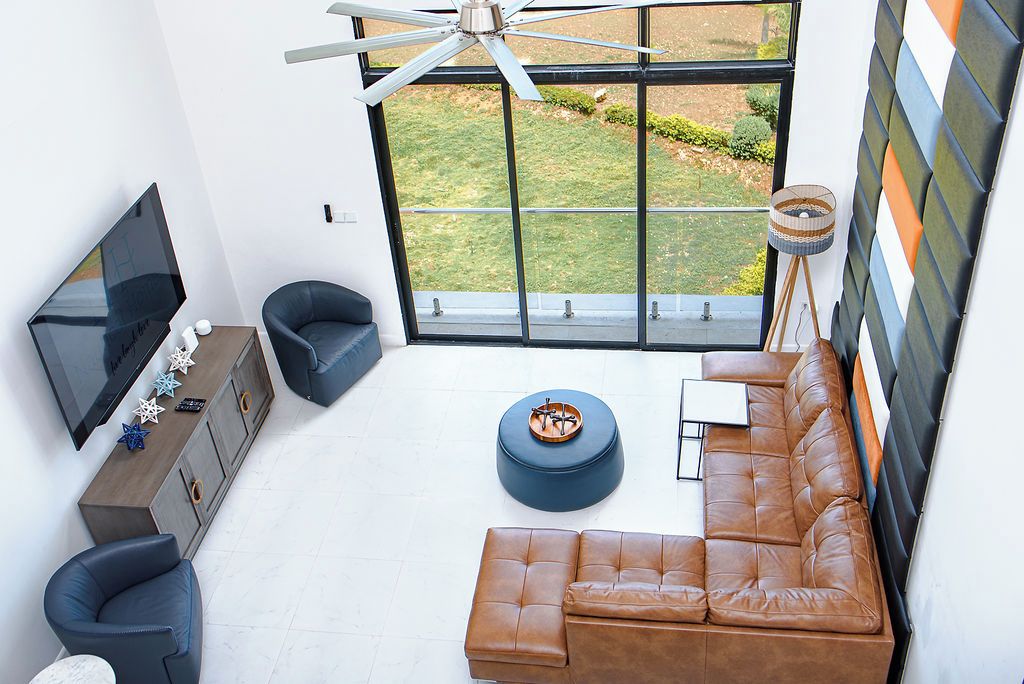 A modern living room with a large TV, leather sofa, and a view of a garden through a large window.