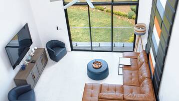 A modern living room with a large TV, leather sofa, and a view of a garden through a large window.