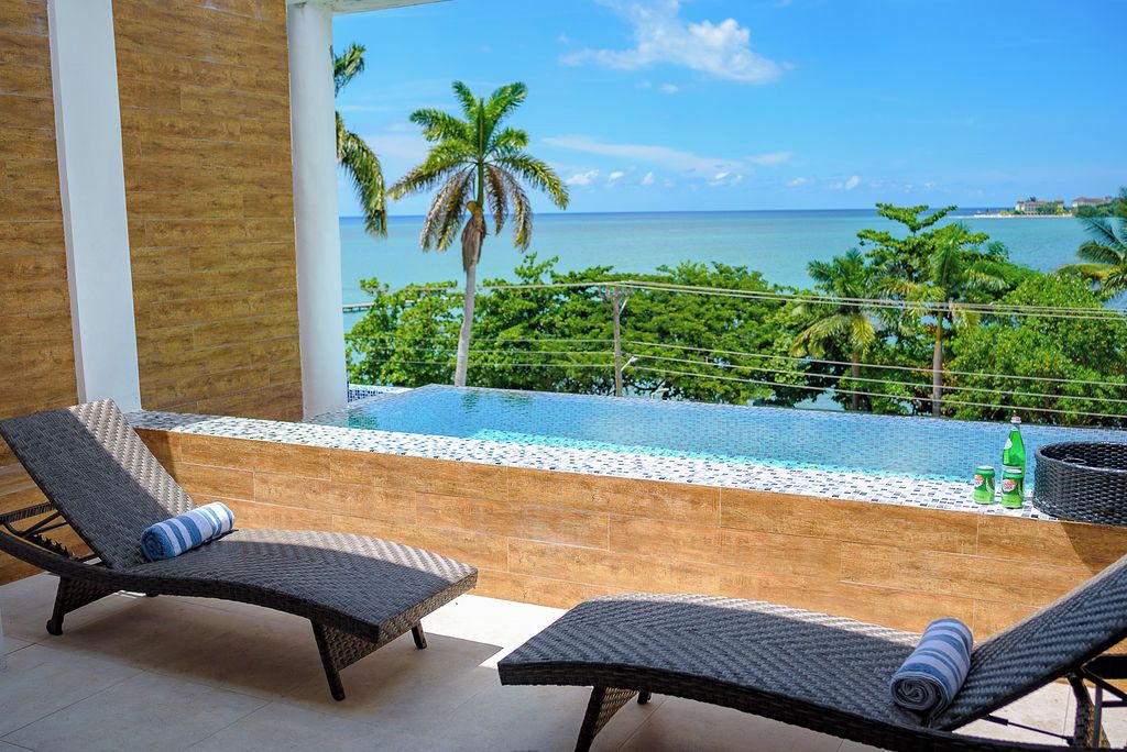 A balcony with two lounge chairs, a small pool, and a view of the ocean.