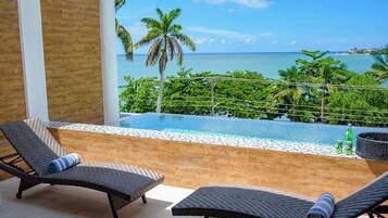 A balcony with two lounge chairs, a small pool, and a view of the ocean.