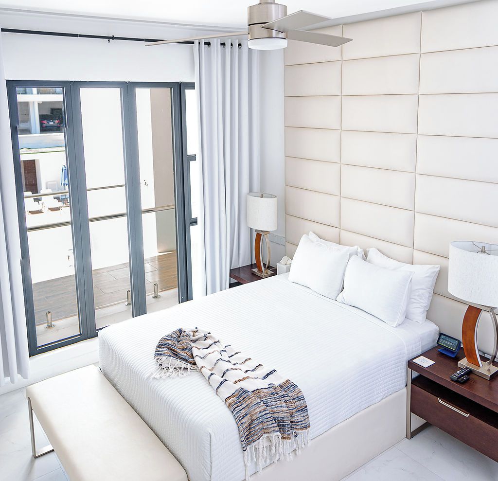 A hotel room with a large bed, a bedside table with a lamp, a bench, and a view of the outside through a sliding door.