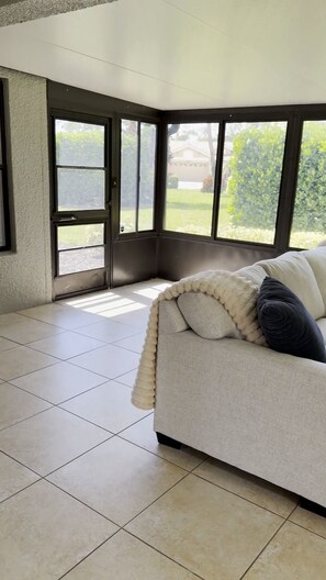 A room with a white sofa, a large window, and a door leading outside. - Florida Retreat in Amenity-Rich Golf & Country Club Community (Bonita Springs)