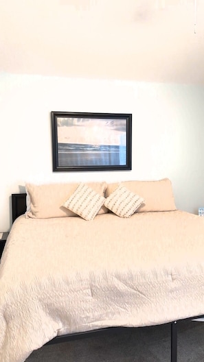 A bed with a beige bedspread and two pillows, a framed picture above the bed, and a nightstand to the left. - Florida Retreat in Amenity-Rich Golf & Country Club Community (Bonita Springs)