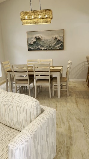 A dining area with a table and chairs, a hanging light fixture, and a wave-themed artwork on the wall. - Florida Retreat in Amenity-Rich Golf & Country Club Community (Bonita Springs)
