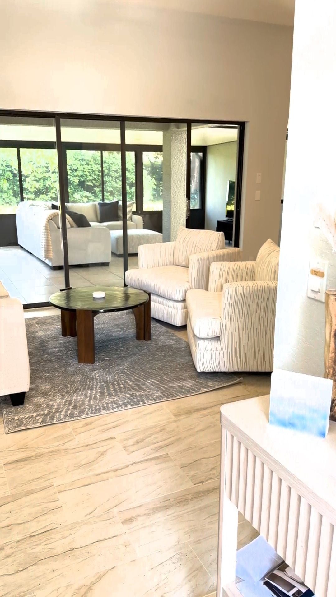 Un salon moderne comprenant un ensemble de canapés, une table basse et une vue sur un espace extérieur, accessible par de grandes portes vitrées.