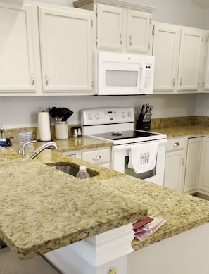 A kitchen with white cabinets, a granite countertop, a microwave, a stove, and a sink. - Florida Retreat in Amenity-Rich Golf & Country Club Community (Bonita Springs)