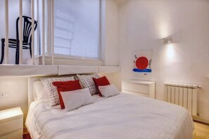 Ein Schlafzimmer mit einem Bett, einem Fenster, einem Heizkörper und einer Wand mit einem Kunstwerk.