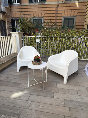 Eine Terrasse mit zwei weißen Plastikstühlen und einem kleinen Tisch, umgeben von einem weißen Metallzaun.
