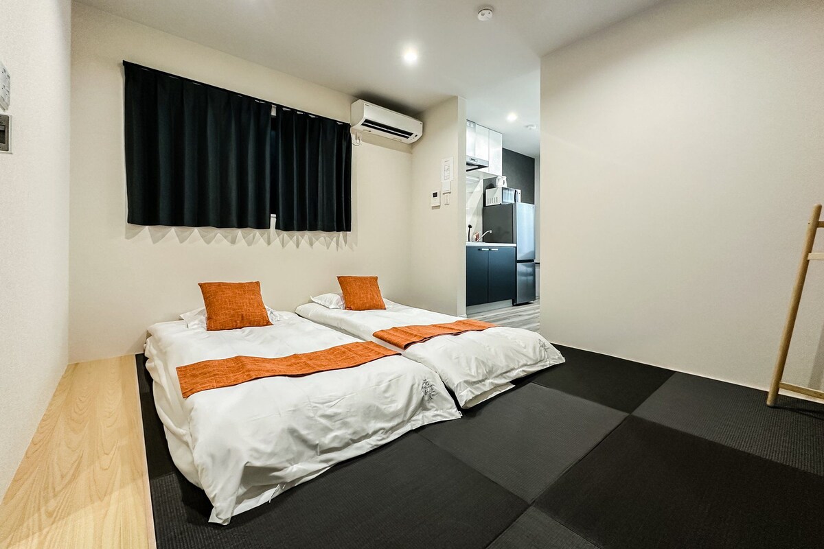 A hotel room with two beds, a small kitchenette, and a bathroom.