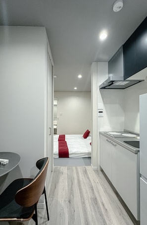 A modern hotel room with a kitchenette, a dining area with a table and chairs, and a bed with red bedding. - HANASTAY MINE (Osaka)