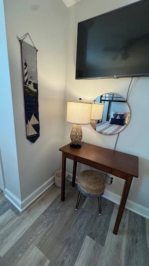 Ein Zimmer mit einem Holztischchen, einem Korbstuhl, einem Wandfernseher und einem Wandbild.