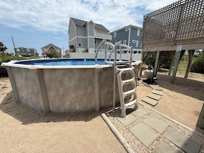 Ein Swimmingpool mit einer Leiter, umgeben von sandigem Bereich und einer Holzterrasse.