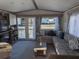 Una sala de estar con sofá, una mesa de centro y televisor. Hay cortinas y vistas al exterior.