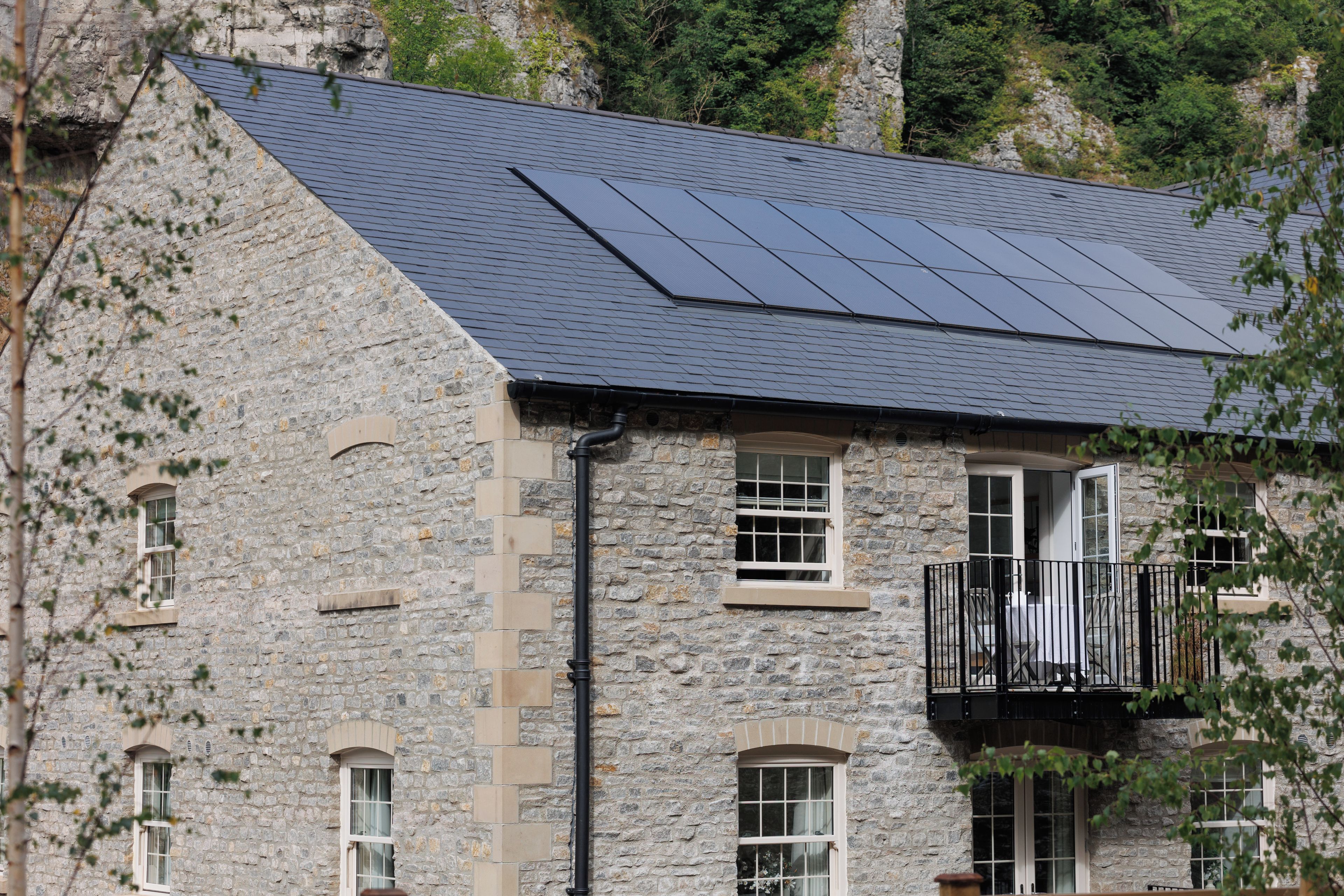 Un edificio de piedra con techo inclinado, paneles solares y un balcón con barandilla negra.