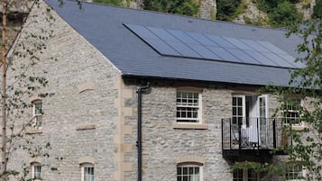 Un edificio de piedra con techo inclinado, paneles solares y un balcón con barandilla negra.