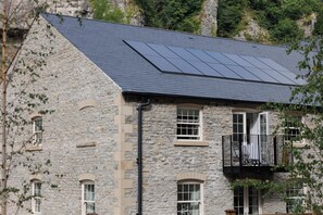 A stone building with a sloped roof, solar panels, and a balcony with a black railing.