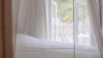 A bedroom with a bed, a window with curtains, and a view of the outdoors.