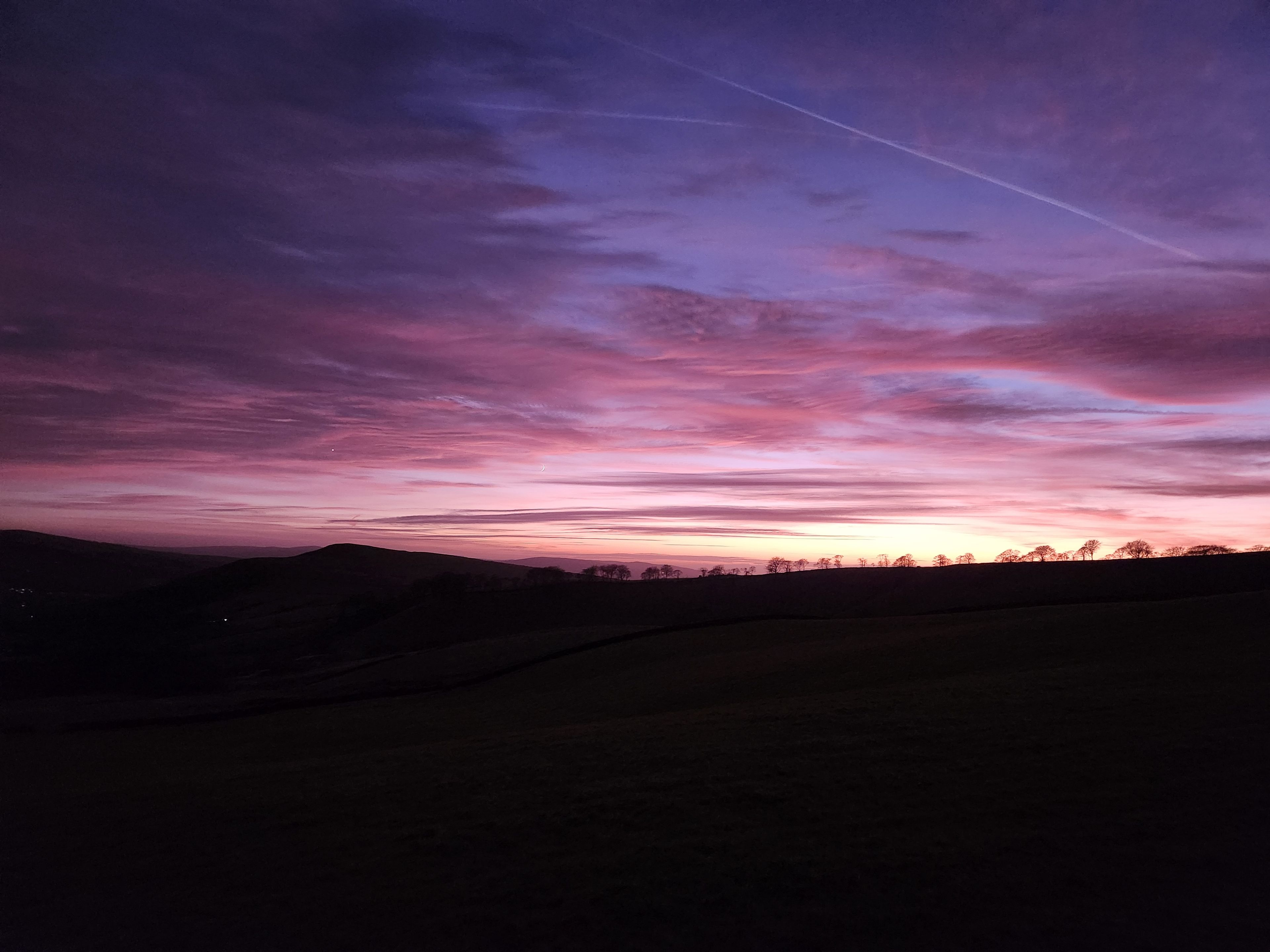 A landscape with a sunset sky, silhouettes of trees, and a distant horizon.