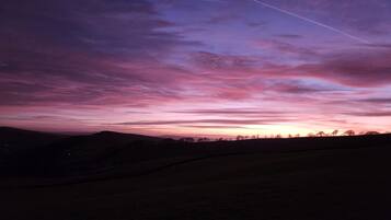 A landscape with a sunset sky, silhouettes of trees, and a distant horizon.