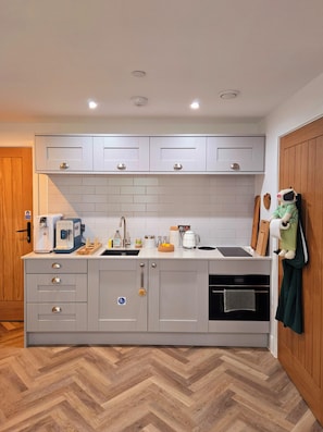 A modern kitchen with grey cabinets, a herringbone wood floor, a coffee machine, and a hanging kitchen towel.
