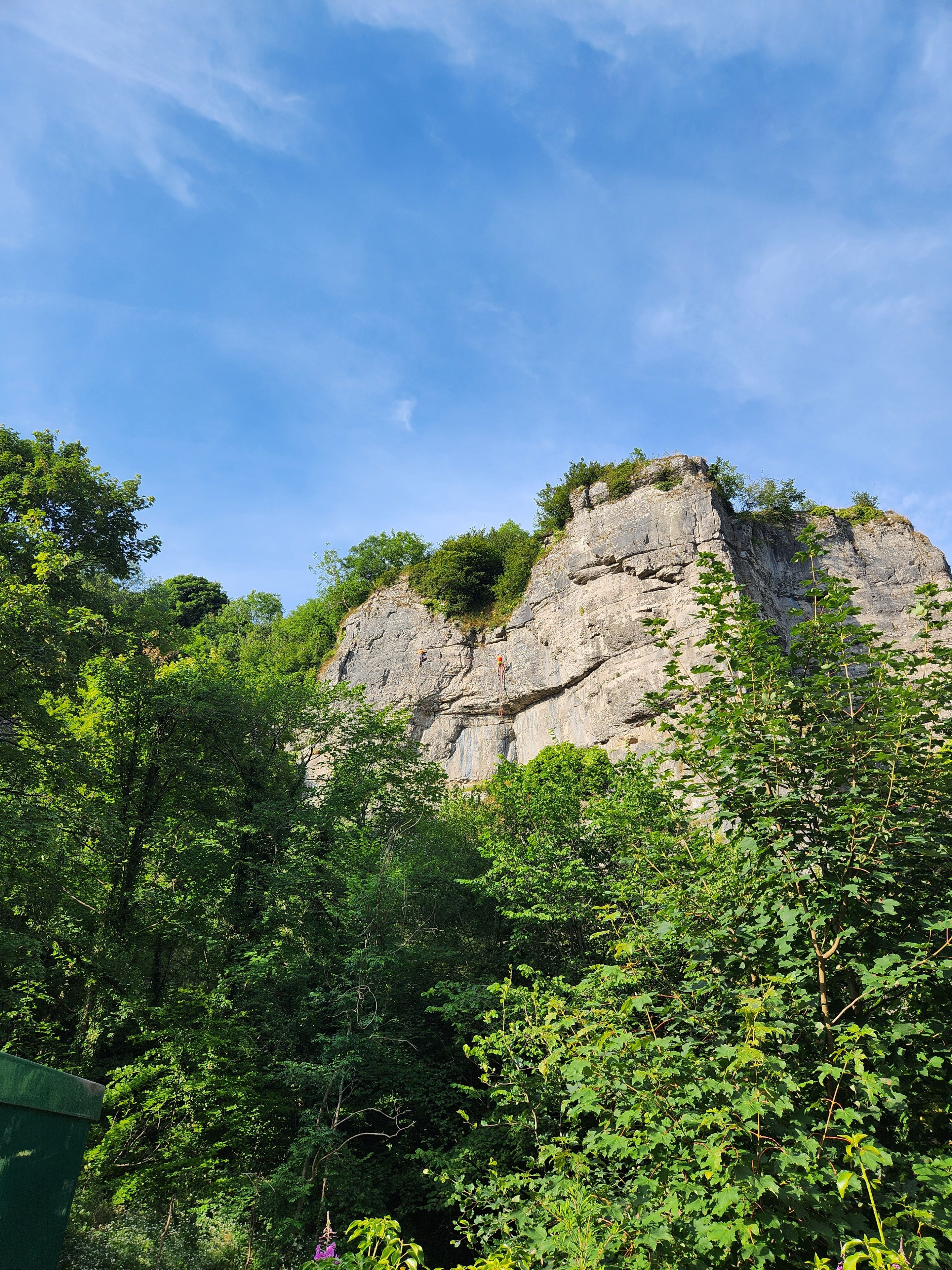En naturlig klippeformation med frodig vegetation i forgrunden.