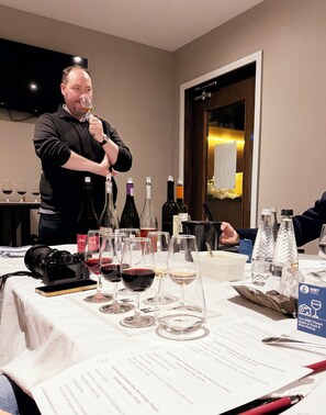 A man holding a wine glass at a table with various bottles and glasses of wine.