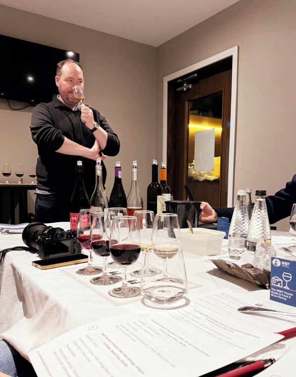A man holding a wine glass at a table with various bottles and glasses of wine.