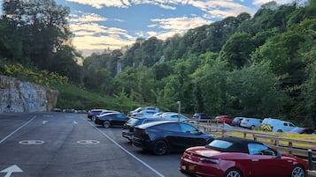 A parking lot with multiple cars, a stone wall, and a forested hillside in the background.