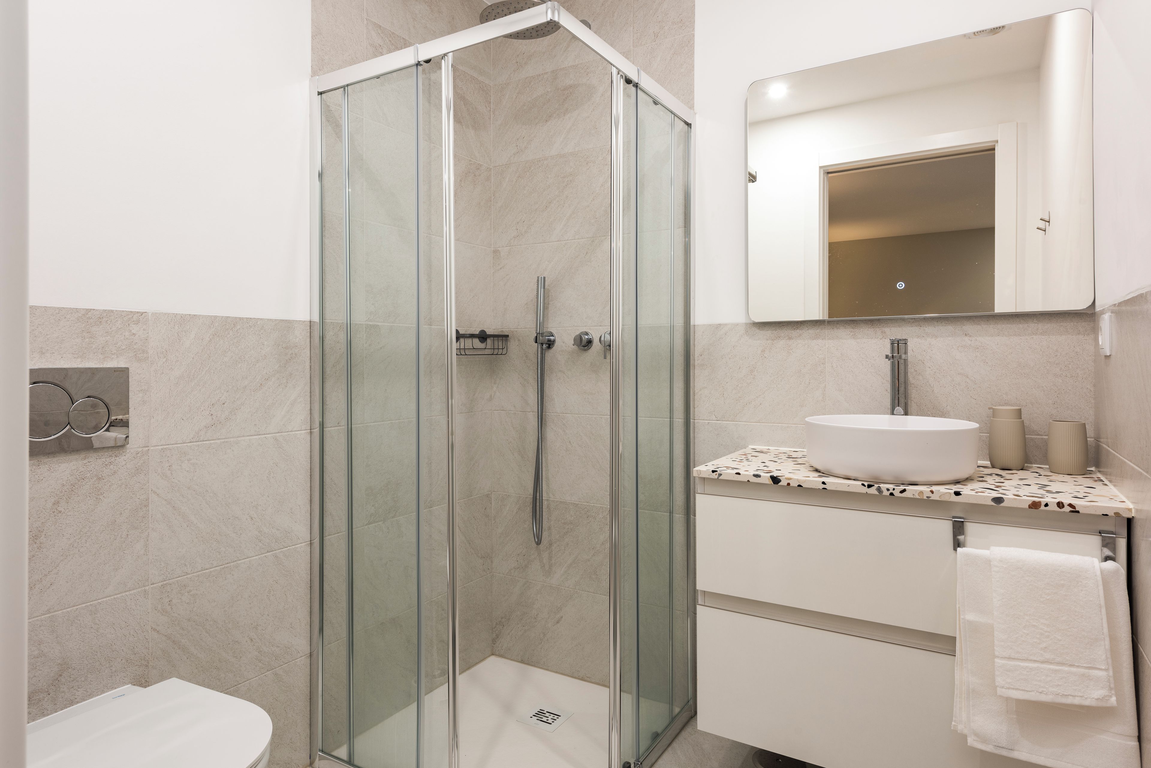 A modern bathroom with a glass-enclosed shower, a white sink, and a mirror above the sink.