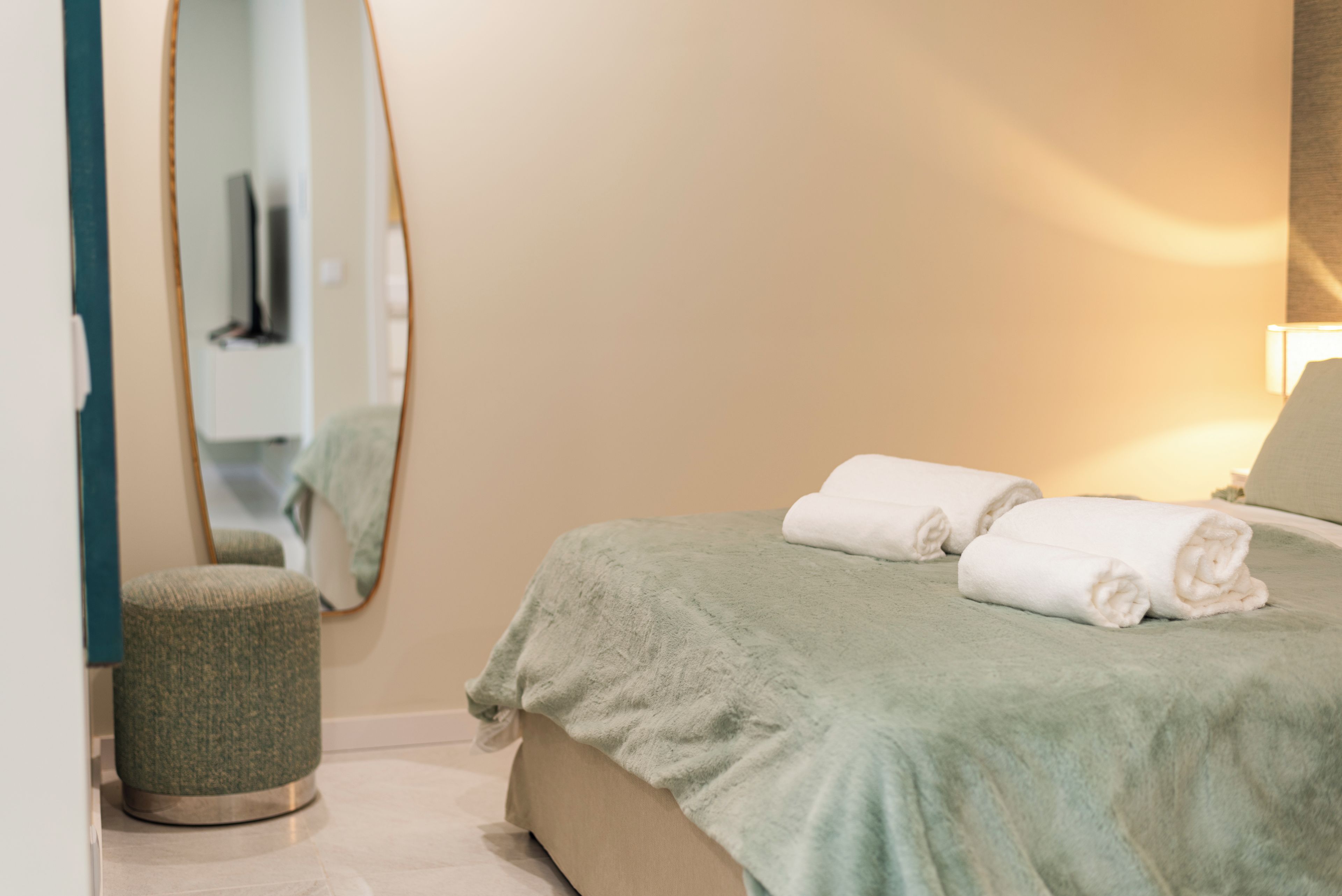 Une chambre à coucher avec un lit, un tabouret rond, un miroir et une lampe.