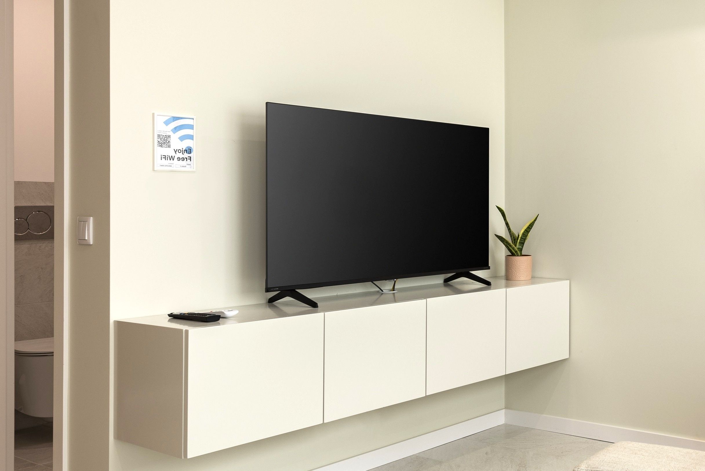 A flat-screen TV on a white cabinet against a wall, with a QR code sign nearby.