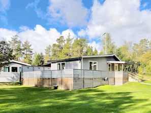 Uma casa móvel moderna no estilo de trailer com um quintal cercado, rodeada por árvores e um céu claro.